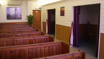 Brown & white funeral ceremony room with pews & smaller curtained funeral rooms off to the side