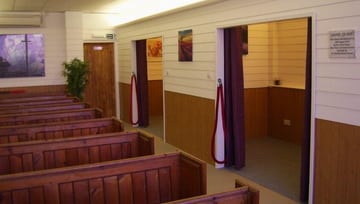 Brown & white funeral ceremony room with pews & smaller curtained funeral rooms off to the side