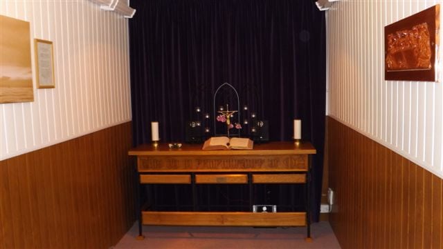 Brown & white funeral room with brown table, candles, book & cross