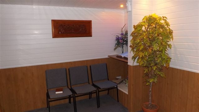 White & brown funeral room with 3 grey chairs up against the wall
