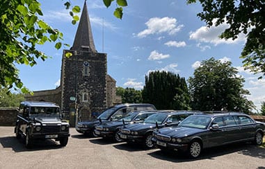 Funeral hearse & Family limo parked outside of a church holding a funeral with T Allen Land Rover is parked on the side of it